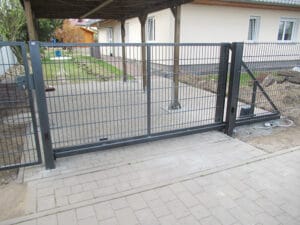 Schwarzes Gartentor aus Metall, Einfahrt mit Pflastersteinen.