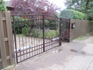 Verschnörkeltes Eisentor und Holzzaun am Einfahrtsweg.