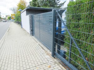 Gehweg neben grauem Metalltor und Hecke.