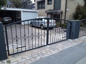 Schmiedeeisernes Gartentor vor Einfahrt mit Auto.