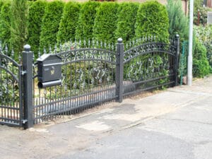 Schmiedeeisernes Gartentor mit Briefkasten und Hecke.