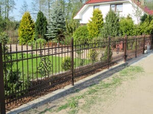 Metallzaun vor einem Garten und Haus.