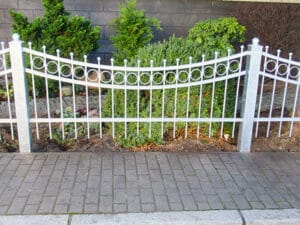 Weiße Gartenzaun vor Hecken und Gehweg.