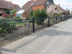 Weg mit Gartenzaun und Wohnhäusern im Hintergrund.