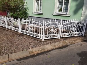 Weißes schmiedeeisernes Tor vor grünem Haus.