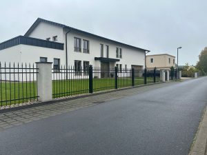 Klassischer Schmiedeeisenzaun mit massiven Steinpfeilern, gefertigt von Komabud – eleganter und langlebiger Zaun .