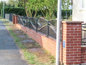 Metallzaun an Backsteinmauer neben Gehweg.