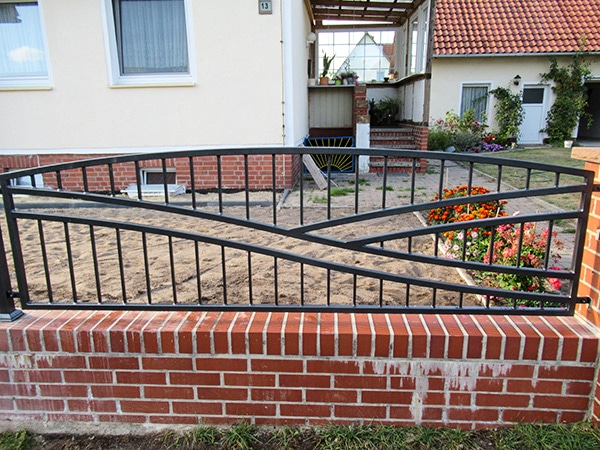 Metallgitter-Zaun auf Ziegelsteinmauer vor Haus.