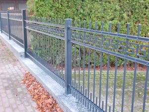Metallzaun an Gehweg mit Hecke.