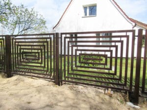 Metallzaun mit geometrischem Muster vor einem Haus.