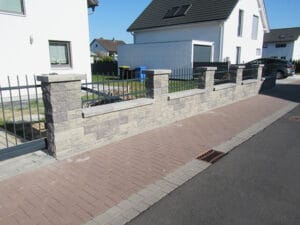 Einfahrt mit Pflastersteinen und Steinzaun in Wohngegend.