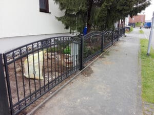 Schmiedeeiserner Zaun entlang eines Gehwegs.