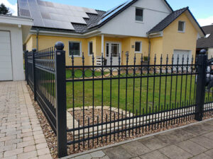 Einfamilienhaus mit Zaun und Solarmodulen auf dem Dach.