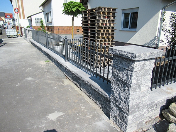 Steinmauer mit Metallzaun in einer Wohnstraße