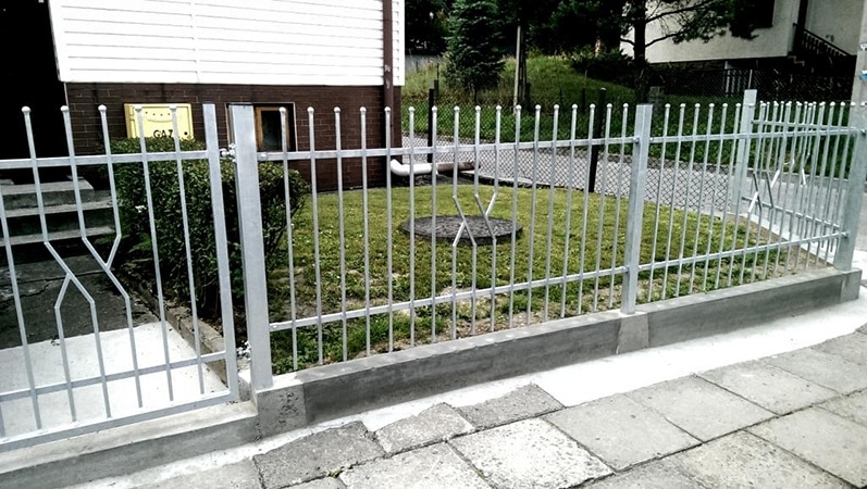 Metallzaun vor einem Wohnhausgarten.