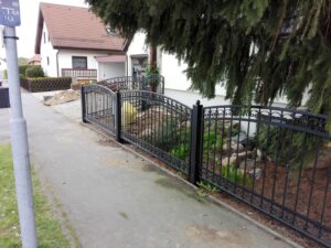 Zierliches, schwarzes Eisentor vor einem Privathaus.