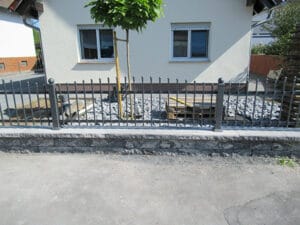 Metallzaun vor weißem Haus mit Baum