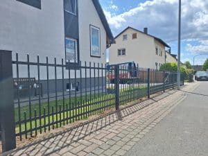 Schmiedeeiserner Zaun mit vertikalen Stäben, montiert vor einem Einfamilienhaus, gefertigt von Komabud