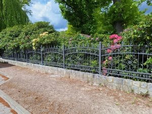 Dekorativer Schmiedezaun mit floralen Ornamenten und geschwungenem Design, montiert auf Natursteinmauer, gefertigt von Komabud