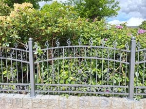 Detailansicht eines Schmiedezauns mit floralen Verzierungen und geschwungener Form, montiert auf Natursteinsockel