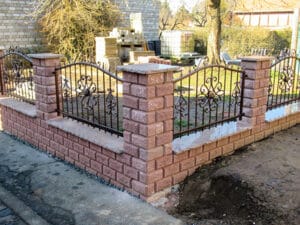 Ziegelsteinmauer mit schmiedeeisernem Zaun im Gartenbau.
