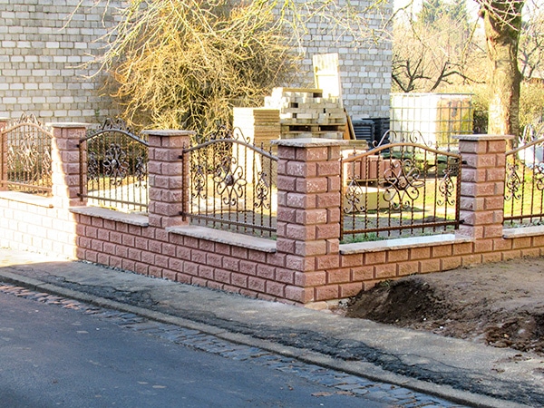 Zaunbau neben Straße mit Ziegelsteinen und Metallgitter.