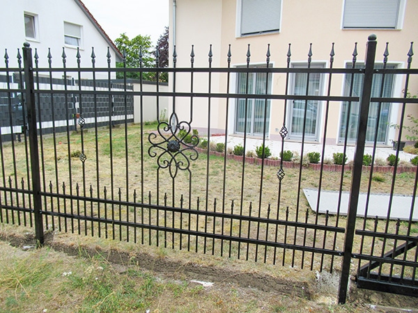 Schmiedeeisernes Tor und Zaun vor einem Haus.