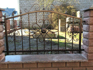 Verziertes schmiedeeisernes Gartentor bei Tageslicht.