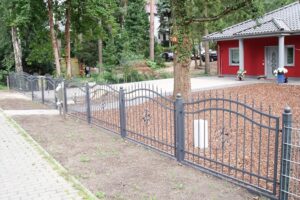 Eisernes Gartentor vor einem Wohnhaus mit Bäumen.