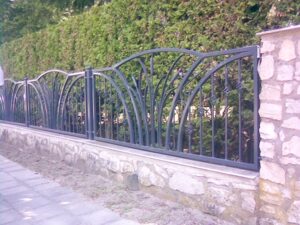 Schmiedeeiserner Zaun an einem Gehweg mit Hecke.