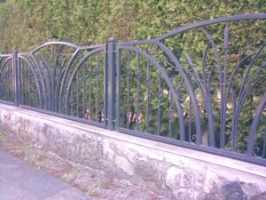 Schmiedeeiserner Zaun vor Hecke.