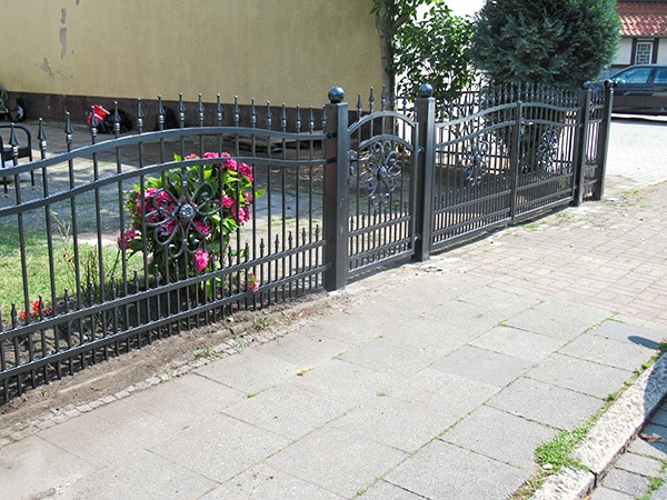 Schmiedeeisernes Tor und Zaun mit Blumen.