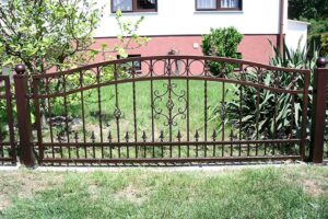 Dekoratives Eisentor vor einem Haus mit Garten.