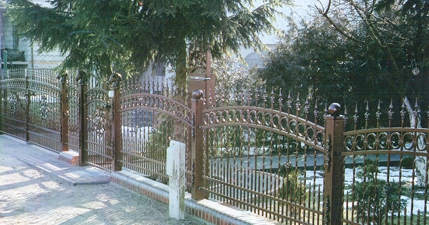 Eisernes Gartentor und Zaun mit Bäumen im Hintergrund.