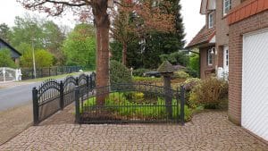 Einfahrt mit schmiedeeisernem Tor und gepflegtem Garten.
