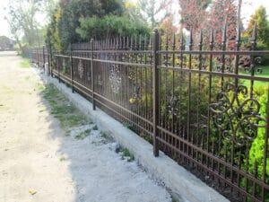 Schmiedeeiserner Zaun an einem Weg mit Bäumen.