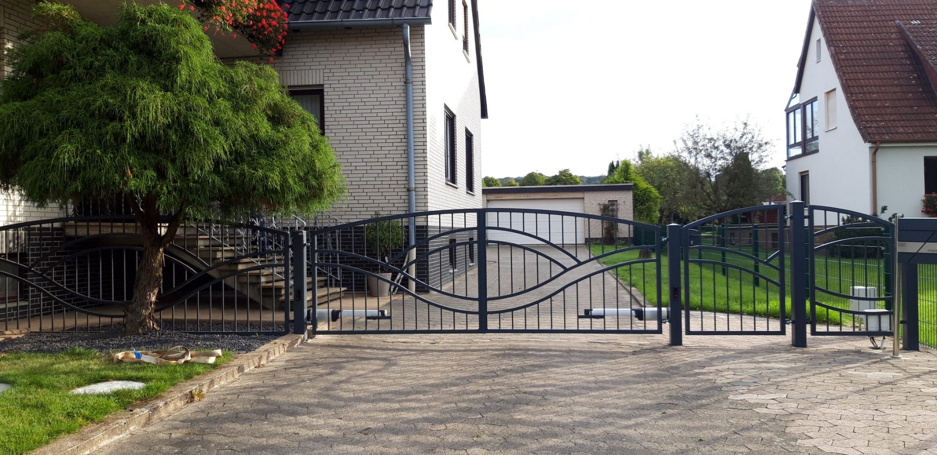 Einfahrt mit geschwungenem Metalltor und Ziegelhaus.