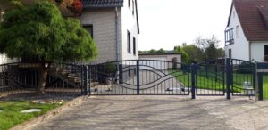 Einfahrt mit geschwungenem Metalltor und Ziegelhaus.