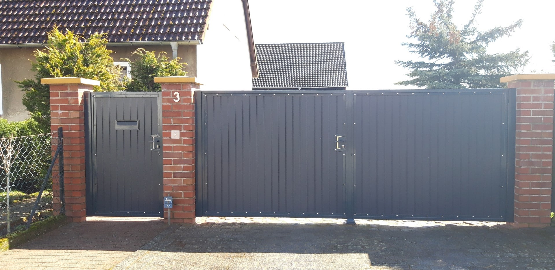 Zaun mit Tor aus Metall und Backsteinpfosten.