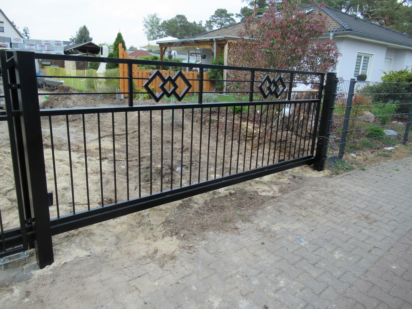 Schwarzes Tor vor Baustelle und Haus.