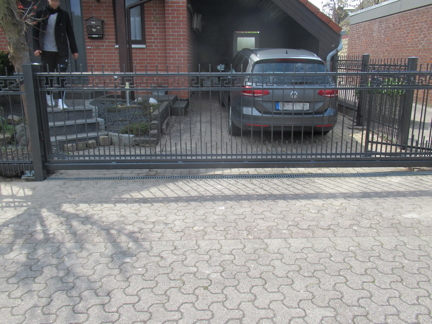 Auto in Einfahrt hinter schwarzem Zaun.