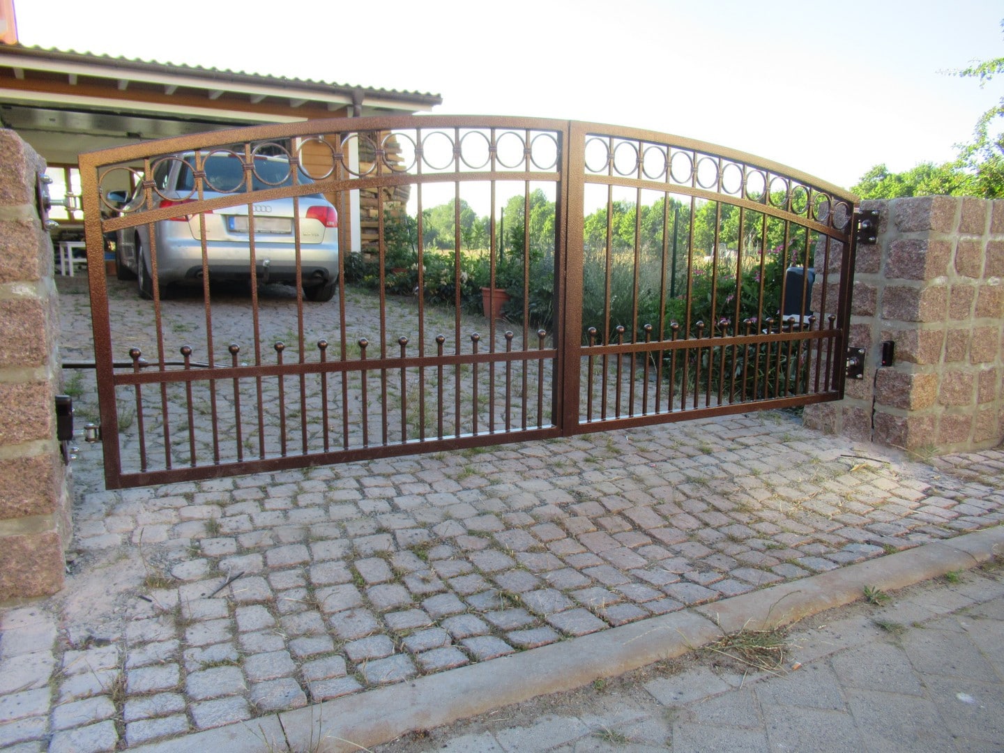 Schmiedeeisernes Tor an gepflasterter Einfahrt.