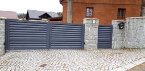 Anthrazitfarbenes Metalltor an Steinpfeilern.