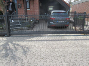 Auto in Einfahrt hinter schwarzem Zaun.