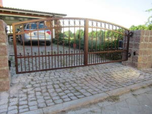 Schmiedeeisernes Tor an gepflasterter Einfahrt.