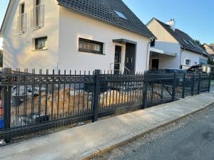 Schmiedeeisernes Tor vor einem weißem Einfamilienhaus.