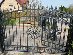 Schmiedeeisernes Tor mit Verzierungen und Gartenblick.