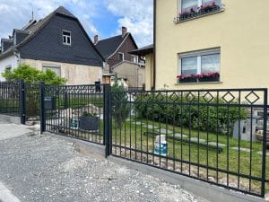 Metallzaun vor Einfamilienhäusern mit Garten.