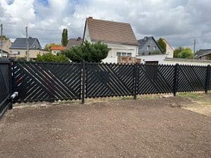 Schwarzer Gartenzaun, Wohnhäuser im Hintergrund.