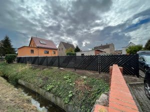 Wolkiger Himmel über ländlichem Wohngebiet mit Zaun und Bach.